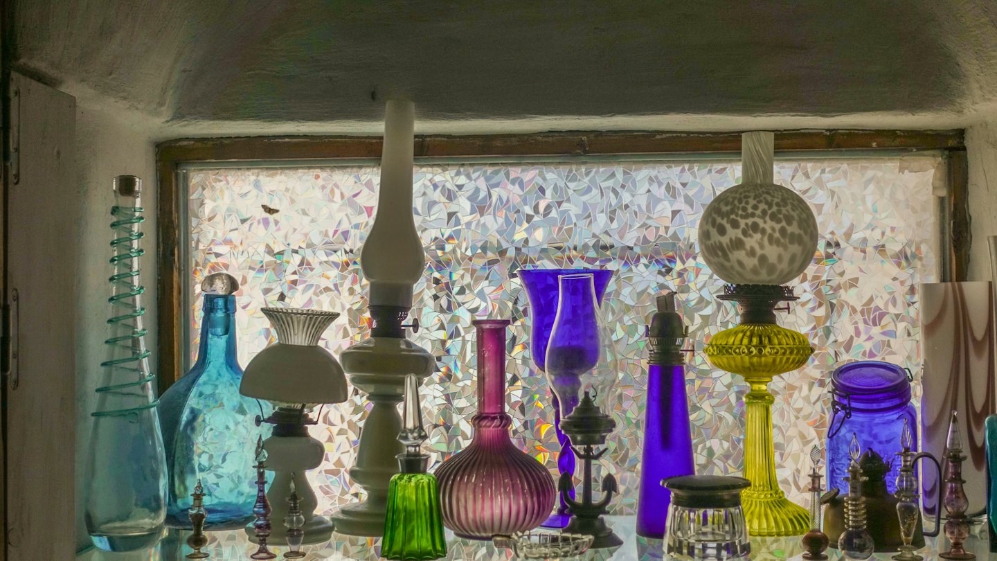 Bottiglie di vetro colorate e lampade a olio vintage su uno scaffale.