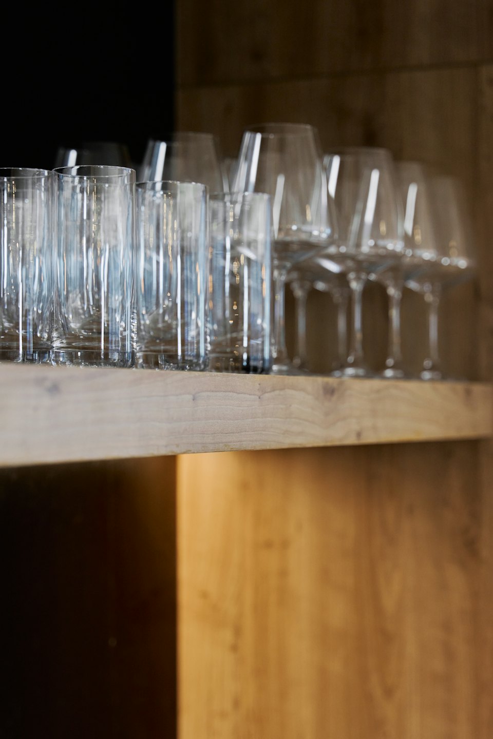 Bicchieri da vino e da acqua trasparenti disposti su una mensola di legno.